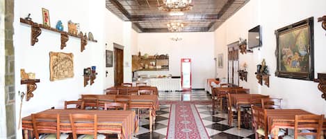 A dining hall with a checkered floor, wooden tables, and chairs, a chandelier, and wall-mounted decorations.