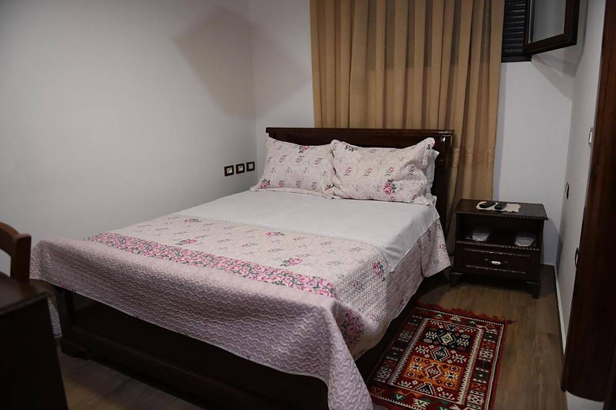 A bedroom with a bed, a nightstand, a chair, and a patterned rug.