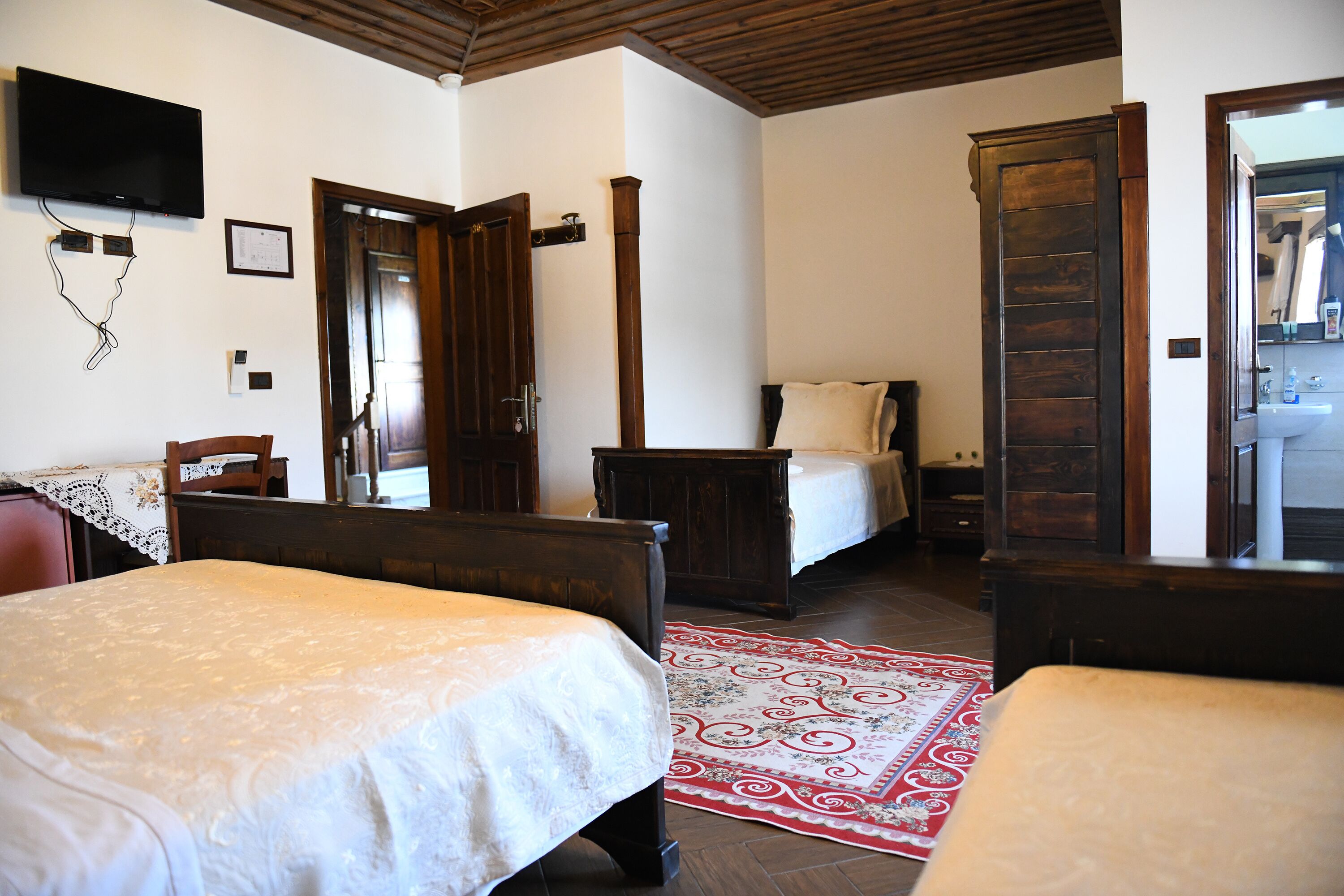Un dormitorio con dos camas, techo de madera, televisión y un baño visible a través de una puerta abierta.