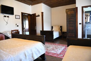 Un dormitorio con dos camas, techo de madera, televisión y un baño visible a través de una puerta abierta.