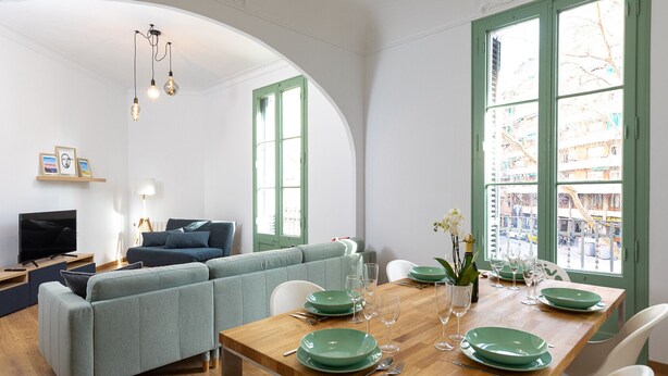 A dining area with a wooden table set for four, green plates, and white chairs. - MODERNIST FAMILY APARTMENT by PriorityVillas (Barcelona)