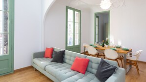 A room with a light blue sofa, green doors, a dining table with chairs, and a chandelier. - MODERNIST FAMILY APARTMENT by PriorityVillas (Barcelona)