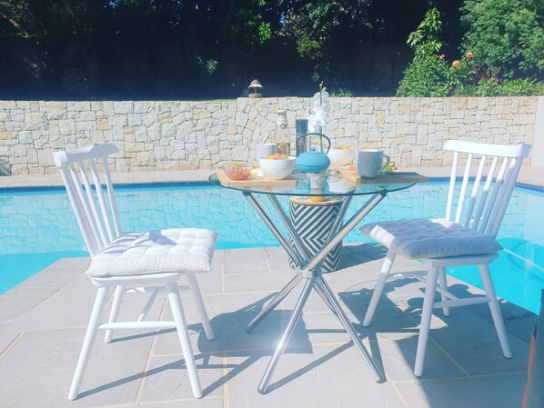 A poolside table with chairs, a stone wall, and a pool.