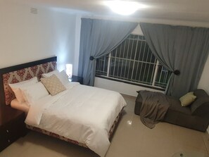 A bedroom with a bed, a nightstand, a sofa, and a window with curtains.
