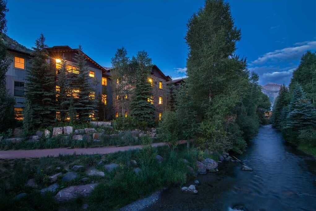 Un chalet comprenant plusieurs bâtiments, une rivière et des arbres environnants.
