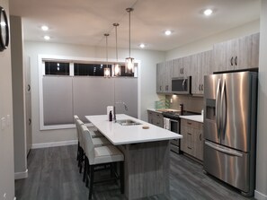 A modern kitchen with a central island, stainless steel appliances, and pendant lighting. - New Home for Business Exec, Professional or Family - Close to U of S and RUH (Saskatoon)