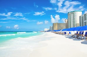 A beach with white sand, clear turquoise water, and blue umbrellas.