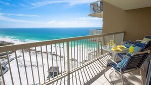 A balcony with a view of the beach and ocean. There is a table with chairs and a small table lamp. - ⛱️Pelican Beach 1915 - Cloud Nine | Gulf Views | 3 Pools⛱️ (Destin)