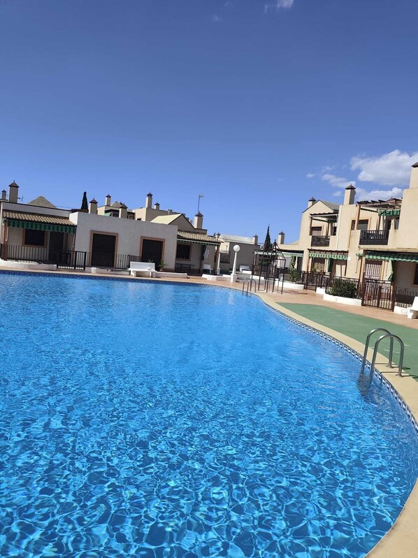 A swimming pool with clear blue water, surrounded by buildings with balconies and a clear sky. - Apartment on the Costa Calida (Puerto de Mazarrón)