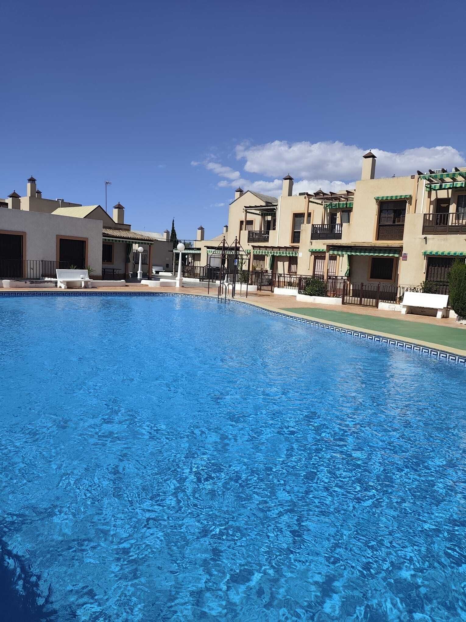 A swimming pool with a clear blue water surface, surrounded by buildings with balconies and a clear sky.