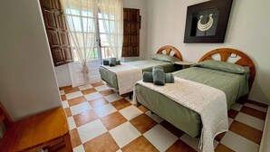 A room with two beds, a wooden headboard, a small table, and a window with curtains.