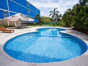 Ein Swimmingpool mit gefliesten Rändern, umgeben von einer Terrasse mit Liegestühlen und einer überdachten Sitzgruppe.