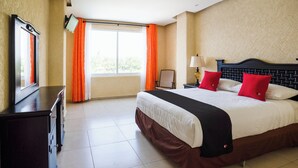 A hotel room with a large bed, a desk, a chair, a TV, and a window with curtains. - Capital O Hotel Los Caracoles, Acapulco (Acapulco)