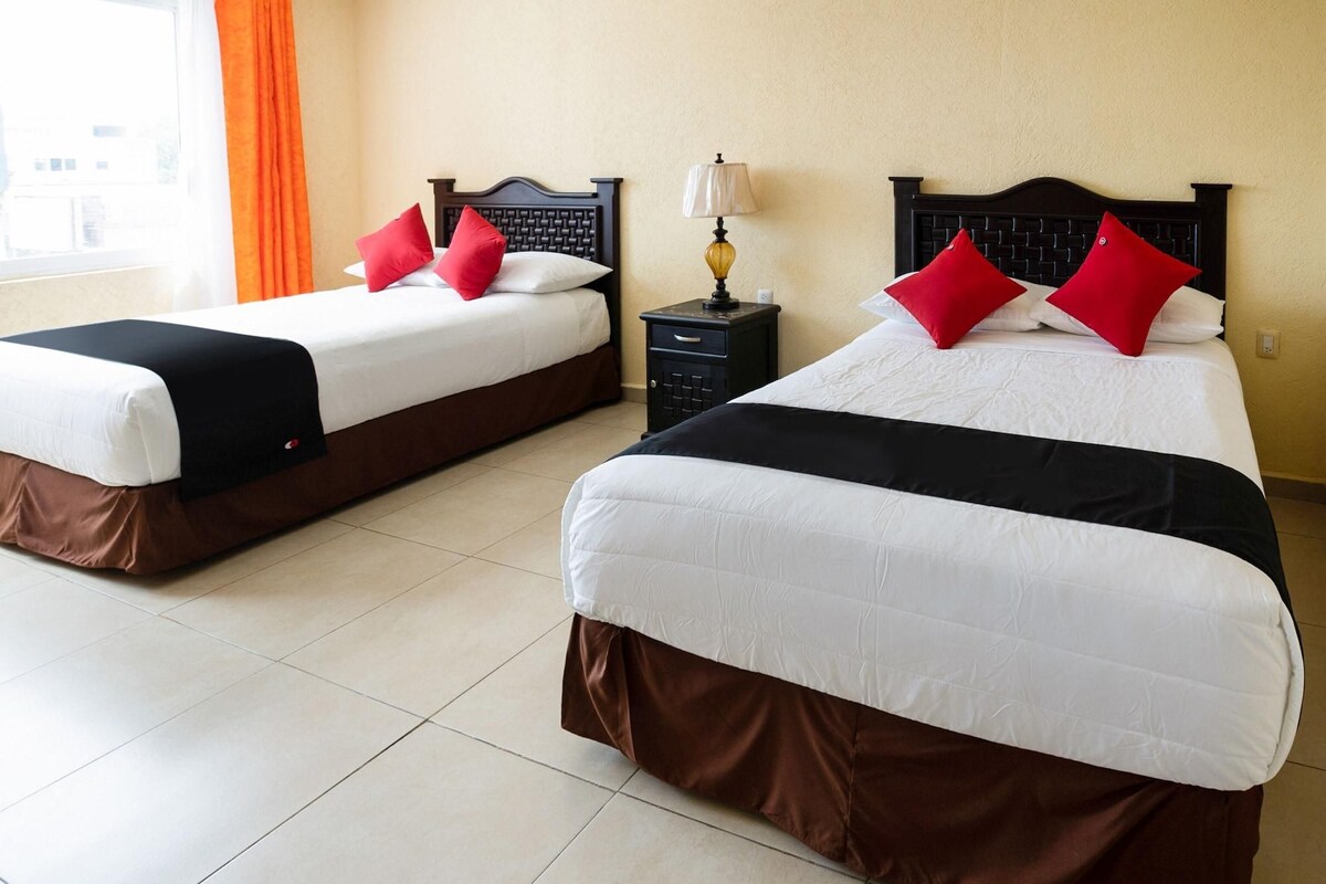 Two twin beds with black and white bedding, red pillows, and a nightstand with a lamp between them.