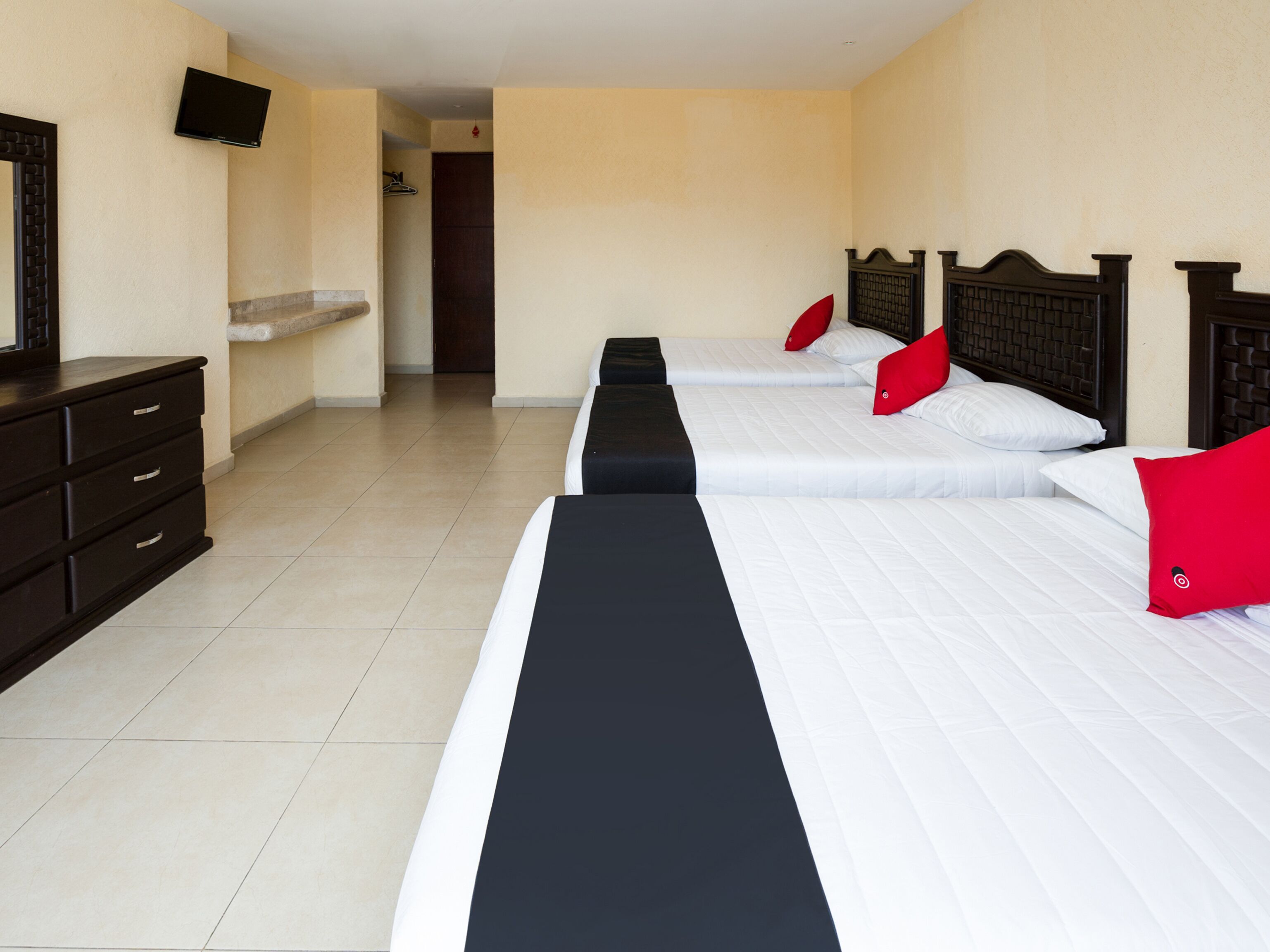 Ein Hotelzimmer mit drei Betten, einem an der Wand befestigten Fernseher und einer Kommode.