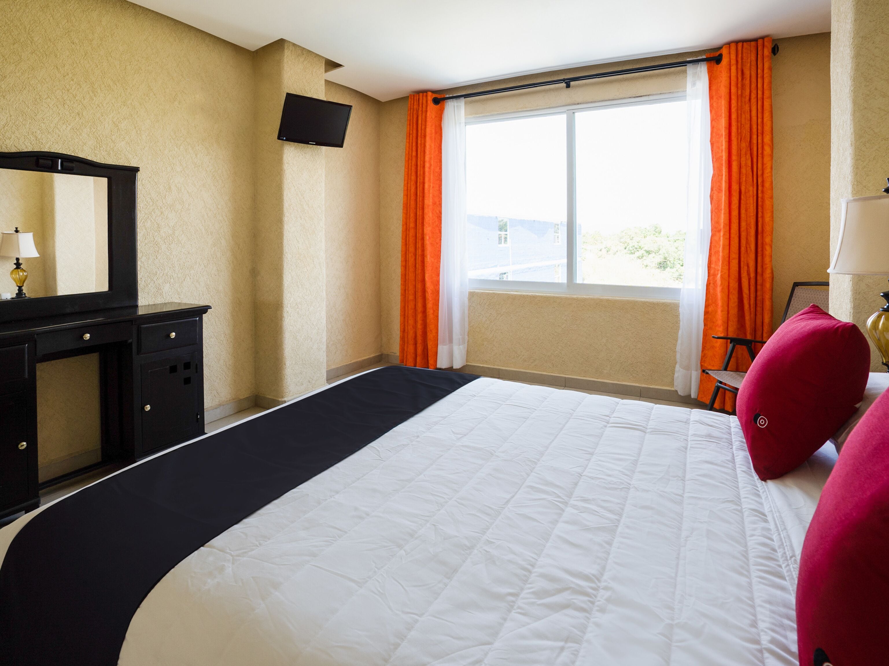A hotel room with a bed, a desk, a chair, a TV, and a window with curtains.