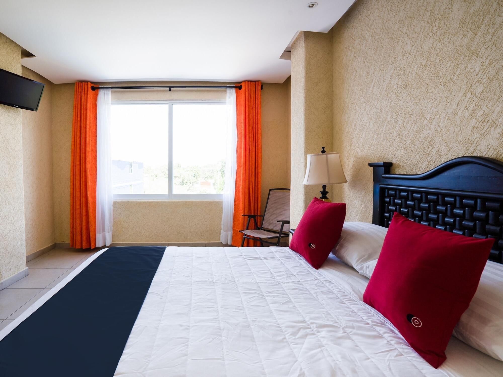 A hotel room with a bed, a chair, a lamp, and a window with curtains.