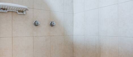 Ducha con azulejos color beige y un cabezal.