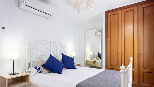 A bedroom with a white bed, blue pillows, a bedside table with a lamp, a wooden wardrobe, and a mirror. - TEBAR BEACH in Playa Blanca (Playa Blanca)