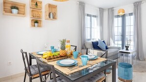 A modern dining area with a glass table, blue plates, and a fruit bowl. There are wooden shelves with plants and a wicker pendant light. - TEBAR BEACH in Playa Blanca (Playa Blanca)
