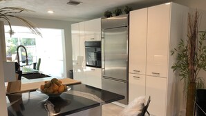 A modern kitchen with a central island, stainless steel appliances, and white cabinetry. - Private Vacation Home w/ Heated Pool. Walk/Bike to Vanderbilt Beach & Amenities. (Naples)