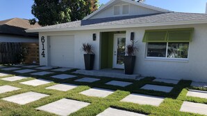 A house with a number '614' on the wall, a front door, two potted plants, and a driveway with a patterned lawn design. - Private Vacation Home w/ Heated Pool. Walk/Bike to Vanderbilt Beach & Amenities. (Naples)