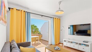 A modern living room with a sofa, coffee table, TV, and a balcony with yellow curtains. - Costa Preciosa - Seaview apartment (Costa Adeje)