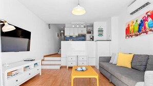 A compact living space with a TV, sofa, coffee table, kitchenette, and stairs leading to an upper level. - Costa Preciosa - Seaview apartment (Costa Adeje)