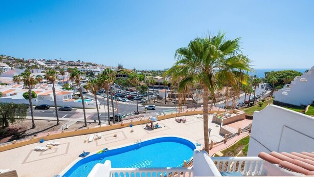 A pool area with a clear view of the surrounding neighborhood, including palm trees and a distant view of the sea. - Costa Preciosa - Seaview apartment (Costa Adeje)