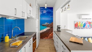 A modern kitchen with a view of a coastal landscape, white cabinetry, and a coffee machine. - Costa Preciosa - Seaview apartment (Costa Adeje)