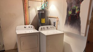 Une buanderie équipée de deux lave-linge Whirlpool, d’un chauffe-eau et d’un seau à serpillière.