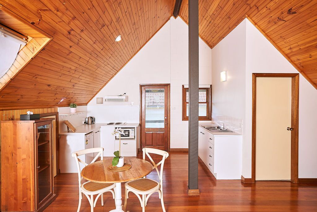 A cozy kitchen with wooden ceiling beams, a dining area with a round table and chairs, and a door leading to another room.