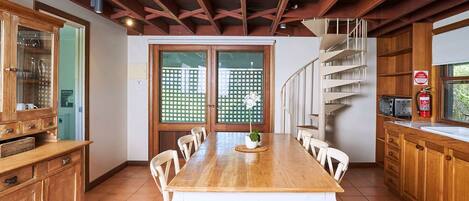 Une cuisine spacieuse avec une table en bois, des chaises blanches et un escalier en colimaçon.