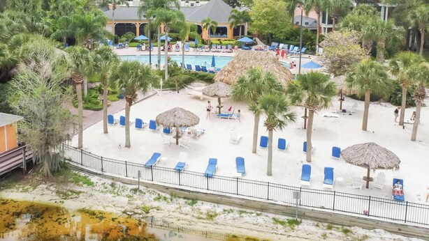Een resort met een zwembad, ligbedden, palmbomen en een klein gebouw.
