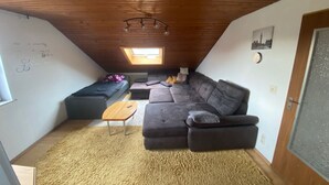 A cozy attic room with a large sectional sofa, a small wooden table, and a skylight. - Large vacation apartment / fitter's apartment on the outskirts of the village in a quiet location (Hochstadt am Main)