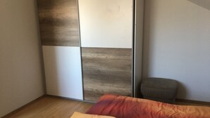 A bedroom with a bed, a wooden wardrobe, and a small ottoman. - Large vacation apartment / fitter's apartment on the outskirts of the village in a quiet location (Hochstadt am Main)