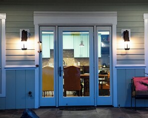 Una puerta principal con un panel de vidrio, un área de comedor con mesa y sillas, y una cocina visible a través del vidrio.