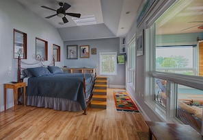Un dormitorio con cama, piso de madera, ventilador de techo, ventana y escalera.