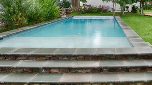 A rectangular swimming pool with a stone border and steps leading up to it.