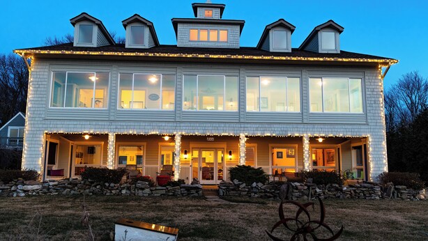 A large, two-story house with multiple windows, a covered porch, and a stone wall in the front yard.