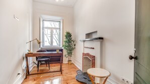 A room with hardwood floors, a wooden desk with a lamp, a potted plant, a fireplace, and a small round table. - Saldanha Pool & Garden (Lisbon)