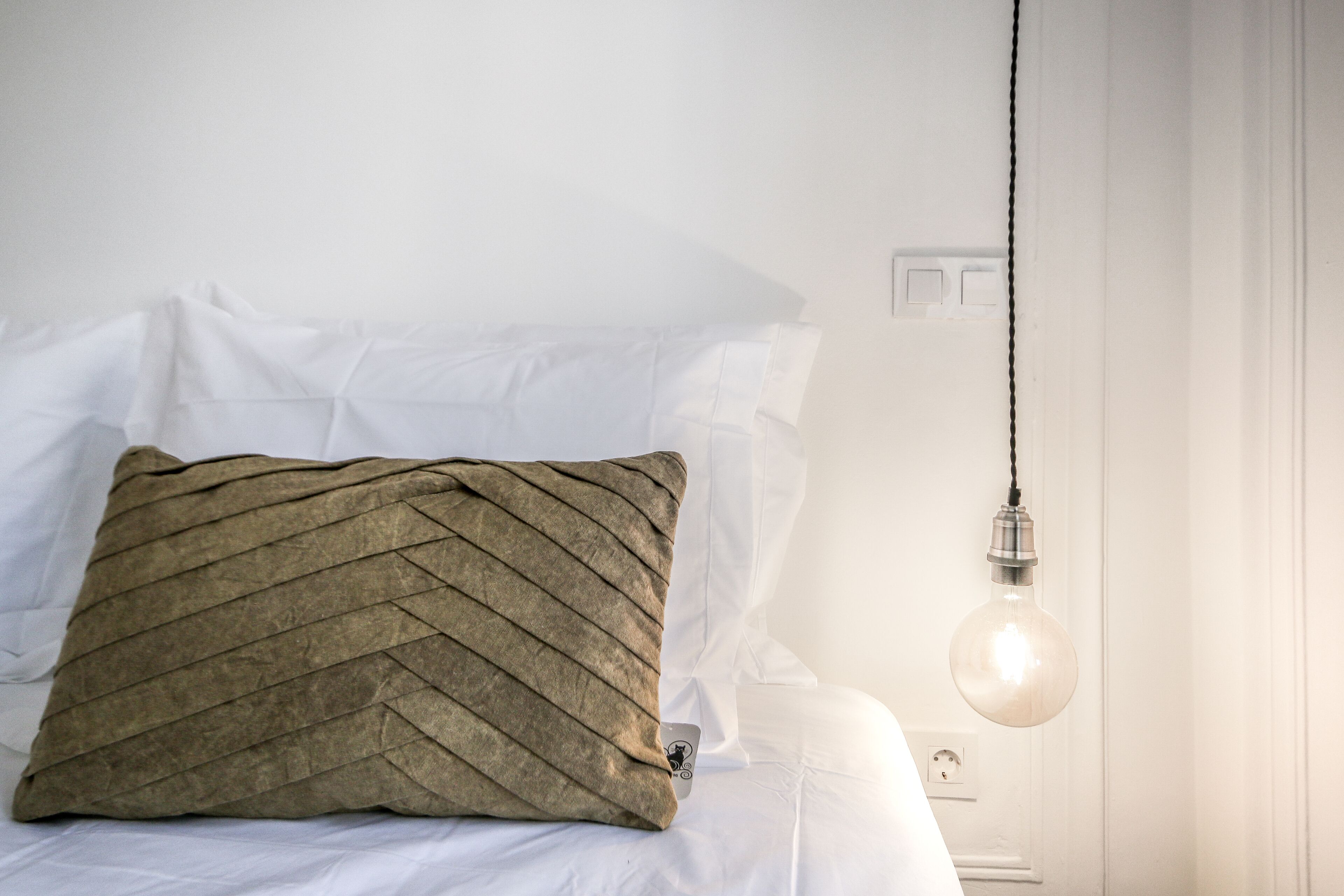 Una cama con un almohadón texturizado y una lámpara colgante.