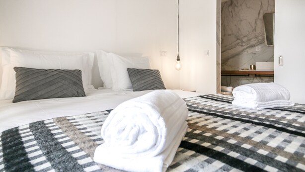 A hotel room with a bed, two pillows, a bedside table, a towel, and a mirror. - Saldanha Pool & Garden (Lisbon)