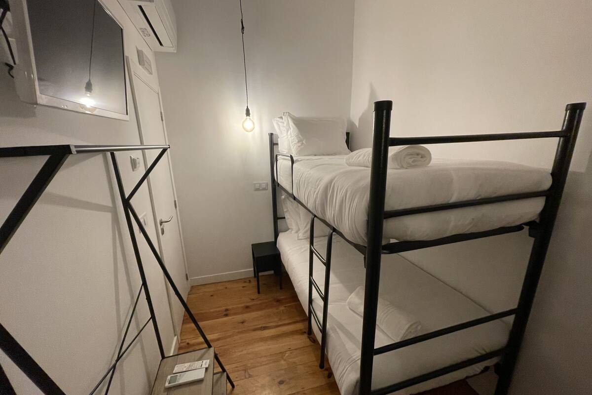 Ein kleines Zimmer mit Etagenbett, einem kleinen Tisch mit einem Gerät und einem Fenster mit einer Lampe.