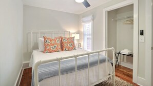 Un dormitorio con cama, ventilador de techo, ventana con persianas y armario con perchero.