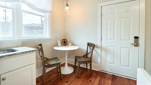 Una pequeña cocina con encimera blanca, dos sillas, una mesa redonda y una puerta blanca.