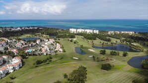 Eine Luftaufnahme eines Golfplatzes mit mehreren Bunkern, Wasserhindernissen und einer Wohngegend mit weißen Gebäuden.