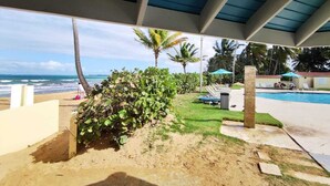 Ein überdachter Außenbereich mit Pool, Liegestühlen und Blick auf Strand und Meer.