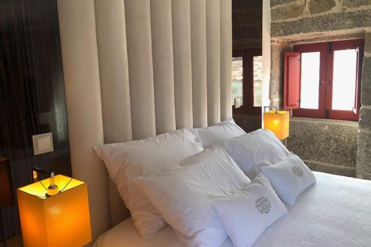 A bed with white pillows and a lamp on either side.