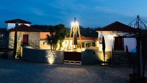 Un edificio in pietra con una porta rossa, un ingresso ben illuminato e una scala che conduce a una zona coperta.